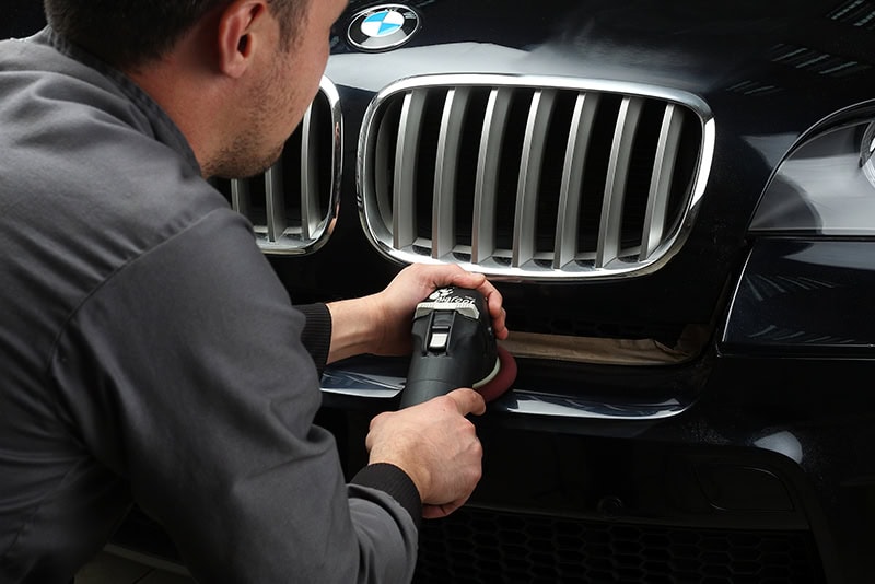 Dent repair technician fixing front grille of luxury BMW vehicle in Denver Dent hail and detail shop.