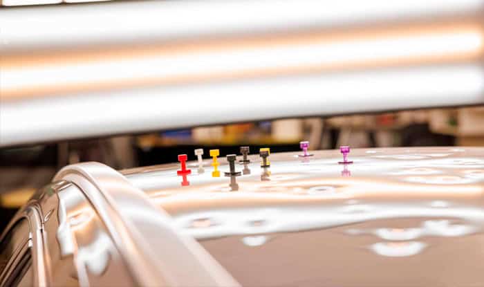 Color-coded pins on a car's roof for dent repair and hail damage restoration in Denver.